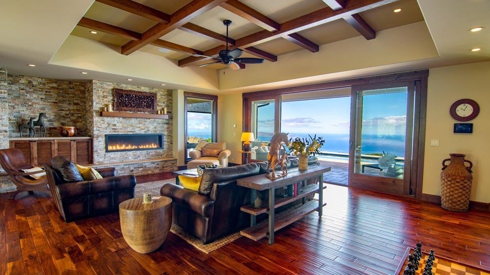Great room with fireplace, open beams, and walls of glass framing the ocean