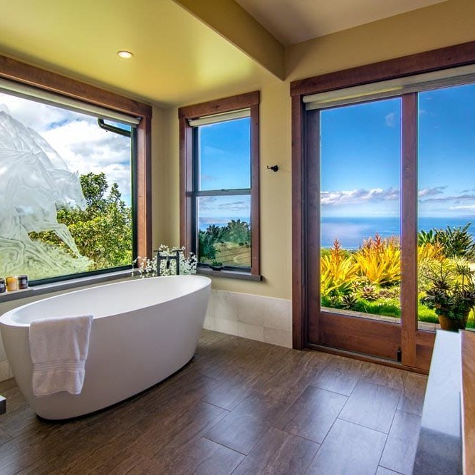Spa bath with a freestanding soaking tub set before a window onto the green mountainside